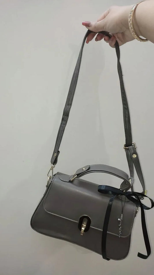 Gray handbag with a black strap held by a hand against a plain background