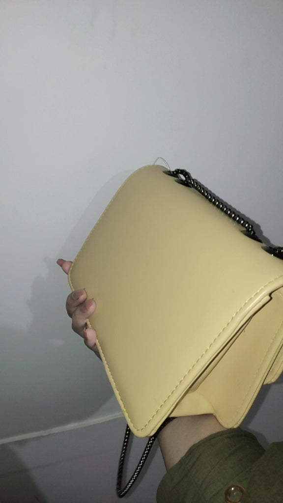Yellow handbag with a chain strap held against a plain background