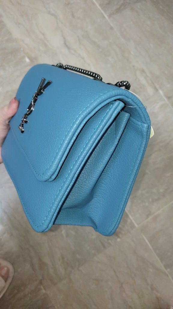 Blue handbag held by a hand on a tiled floor background