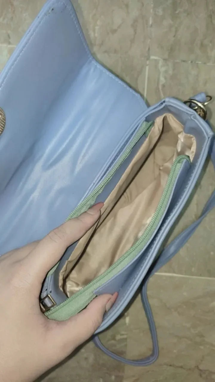 Hand holding a light blue handbag with a beige interior on a tiled floor.
