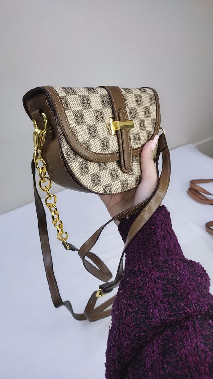 Hand holding a patterned handbag with a gold chain on a white surface