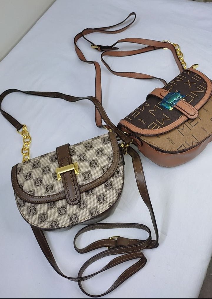 Two handbags, one patterned and one plain, on a white surface with a curtain in the background.