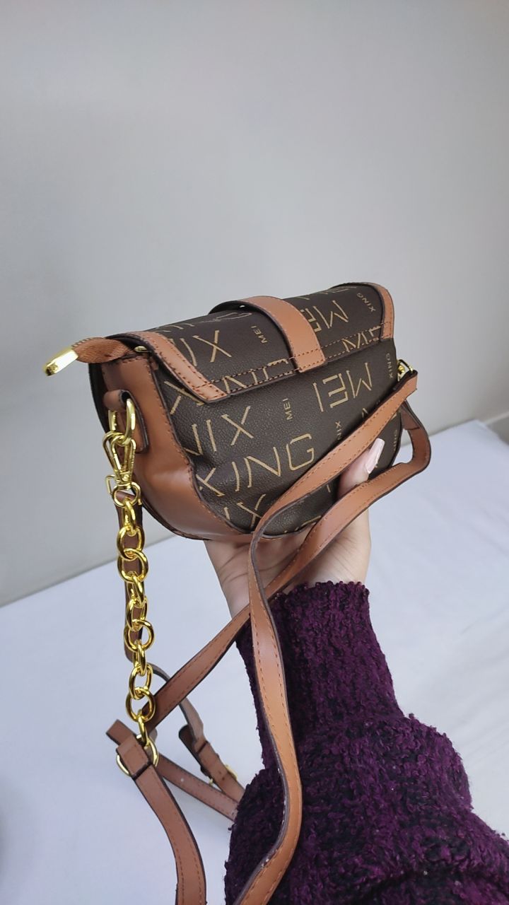 Brown handbag with gold accents held open by a hand, with a visible brand tag.