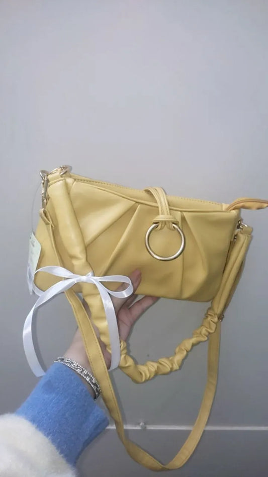 Yellow handbag with a ring handle held by a person against a gray background