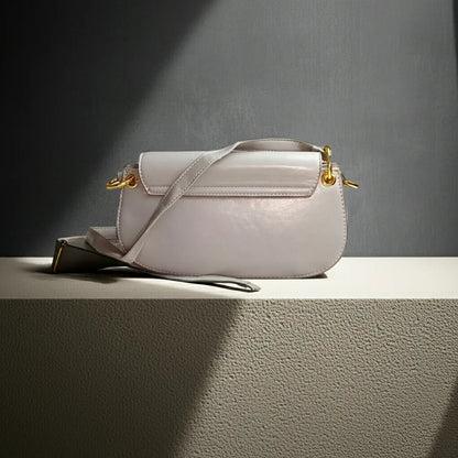 Light gray handbag with gold accents on a textured surface