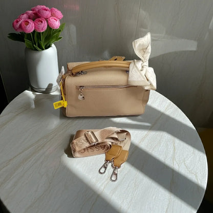 Beige handbag with matching strap on a marble surface, next to a vase of pink flowers.