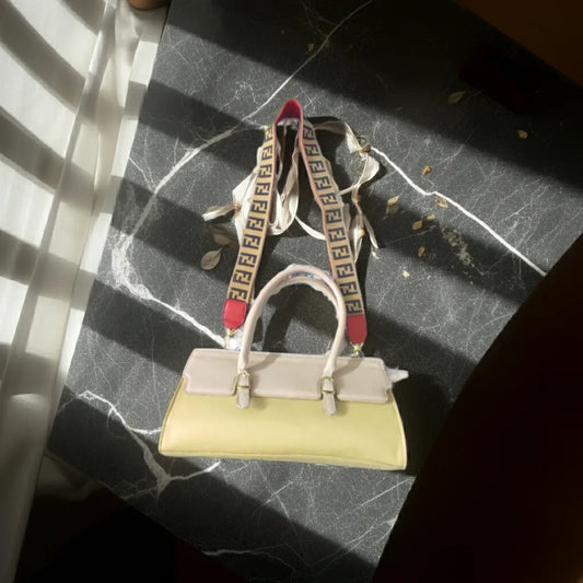 Light-colored handbag with a patterned strap on a dark marble surface